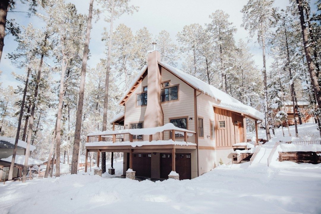 Snötäckt fjällstuga bland tallar med terrass och garage